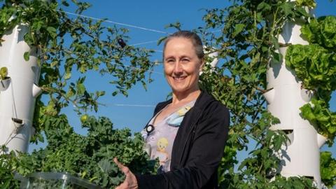 A woman stands holding a container overflowing with freshly picked lettuce