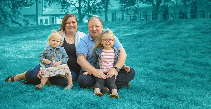 Family with parents and two children posing in an outdoor space with a teal background